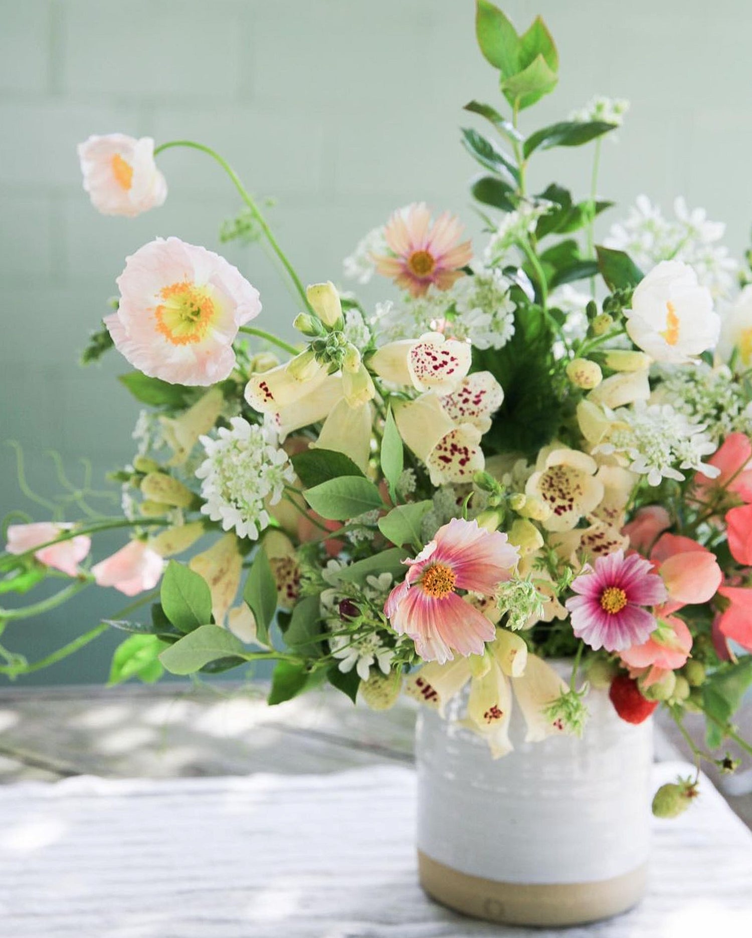 Pink and yellow spring flower arrangement made with foxglove, cosmos and poppies in a handmade ceramic vase