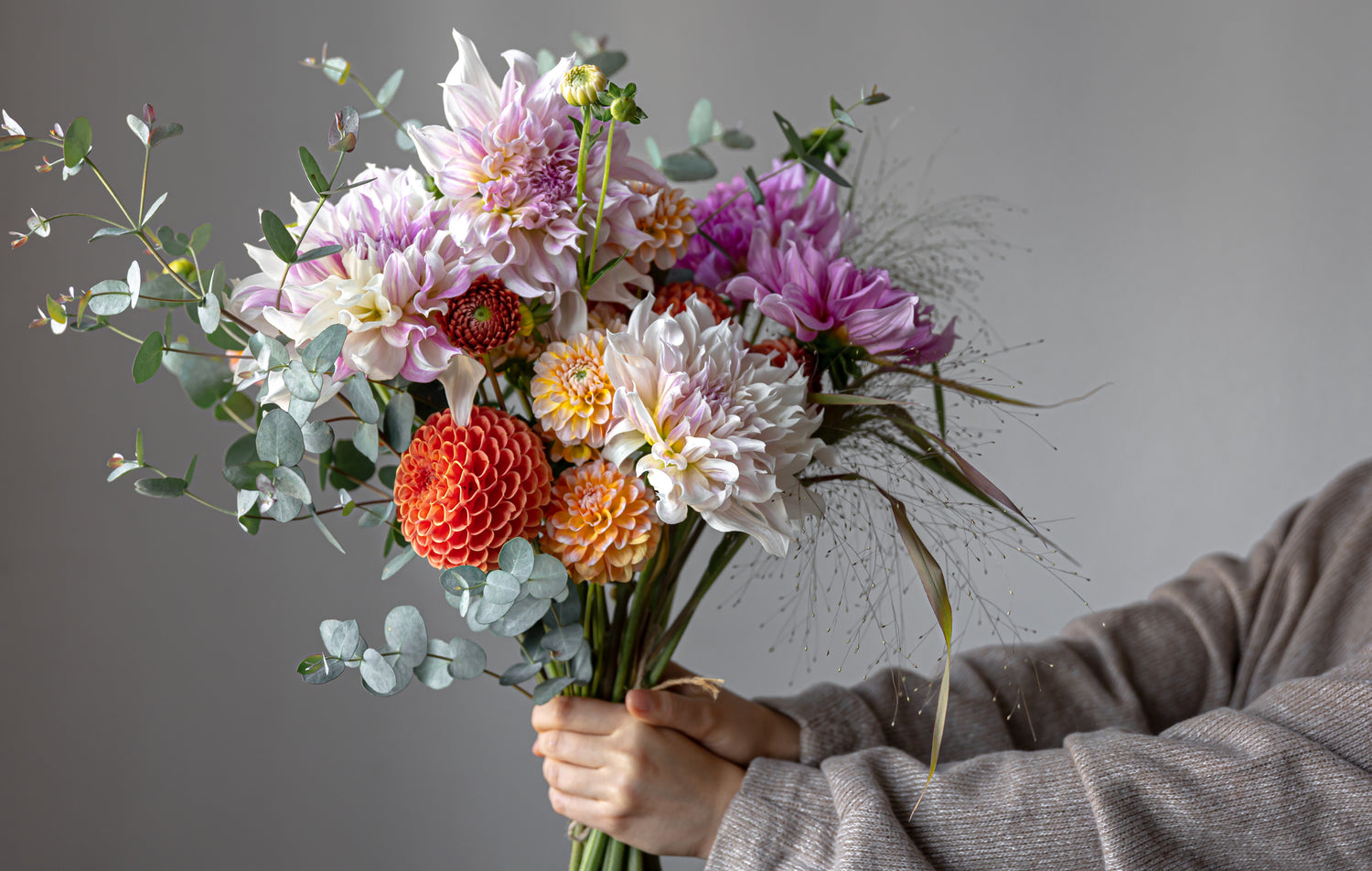 Florist holding a bouquet of pink and orange dahlias with eucalyptus accents