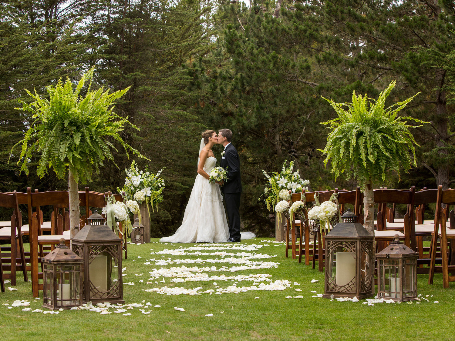 Outdoor wedding at Poppy Hills Golf Course in Pebble Beach with bride in white and groom in black tuxedo at the alter in front of a grove of pines