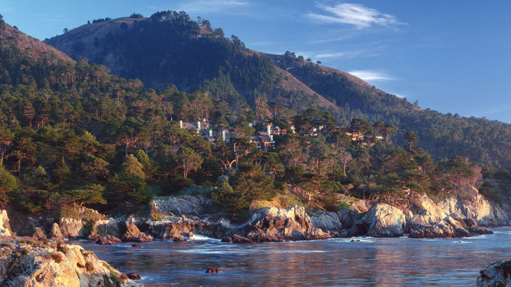 Panoramic view of Carmel Highlands showing a rocky beach and Hyatt Carmel Highlands Inn tucked into the wooded cliff